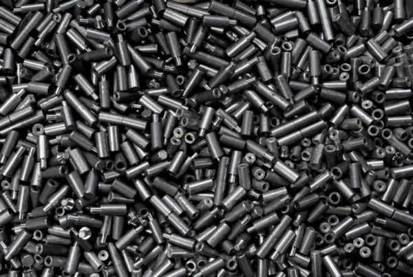 A large pile of small, cylindrical metal pieces with holes on top, appearing random but uniformly placed, showcases the precision possible with metal additive manufacturing.