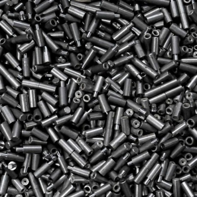 A large pile of small, cylindrical metal pieces with holes on top, appearing random but uniformly placed, showcases the precision possible with metal additive manufacturing.