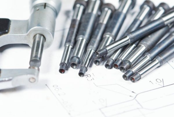 Close-up of a micrometer and several precision metal rods on a technical drawing paper.