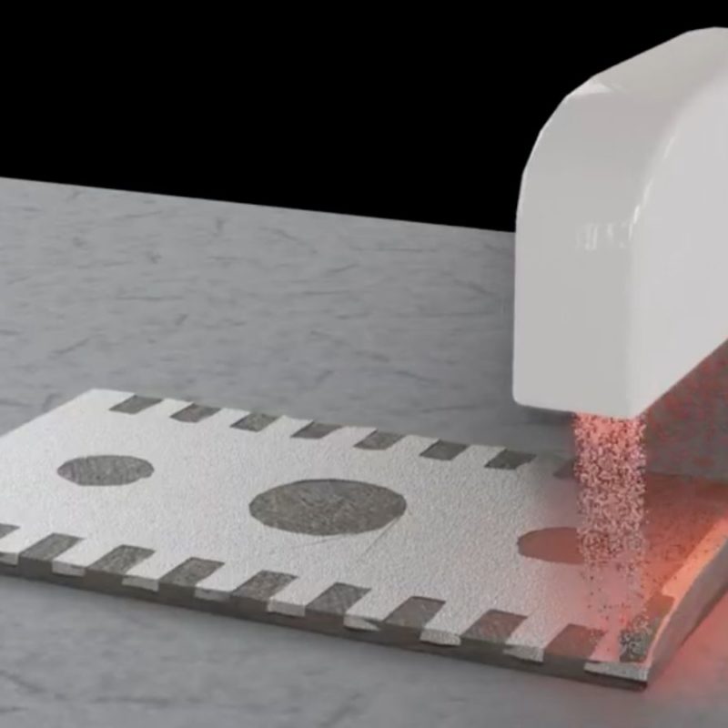 A white machine prints a circuit onto a metal surface using a red laser in a process demonstration.
