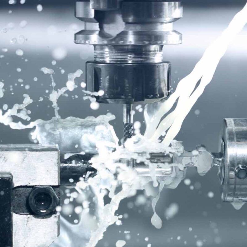 Close-up of a CNC machining process, with cooling fluid being sprayed onto a metal workpiece as it is being shaped on a lathe.