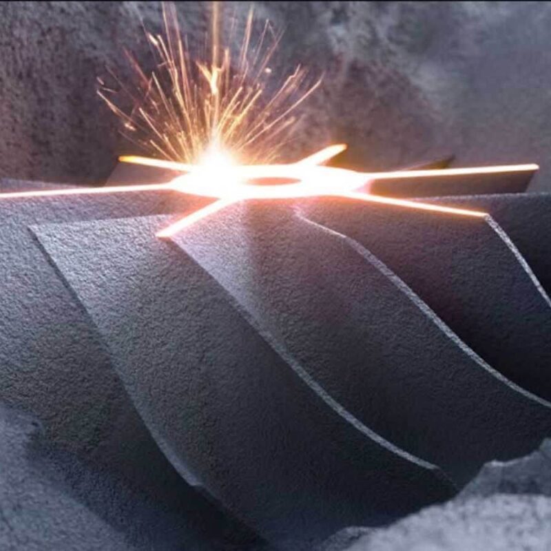 A metal object with a complex geometric shape is being worked on by a laser, emitting sparks in an industrial setting.
