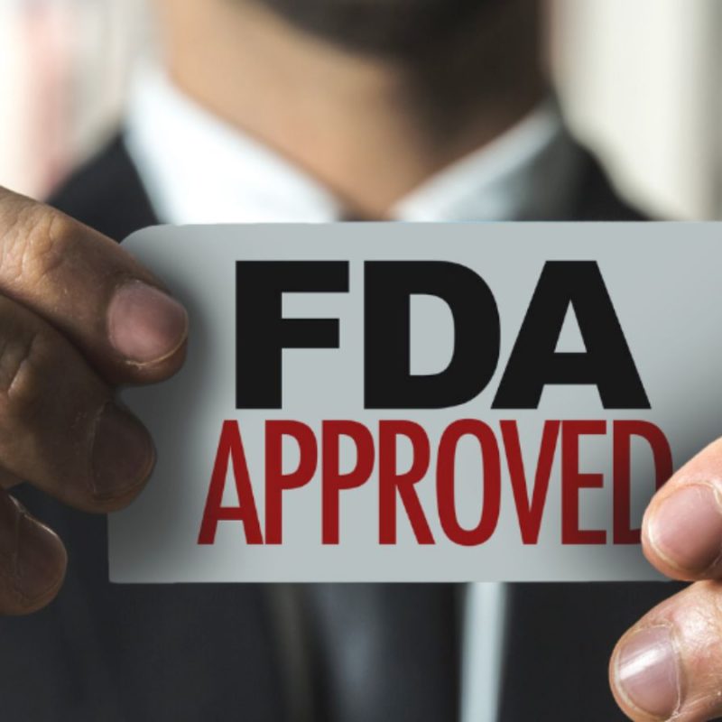 A person in a suit holds up a card with the text "FDA APPROVED" written on it.