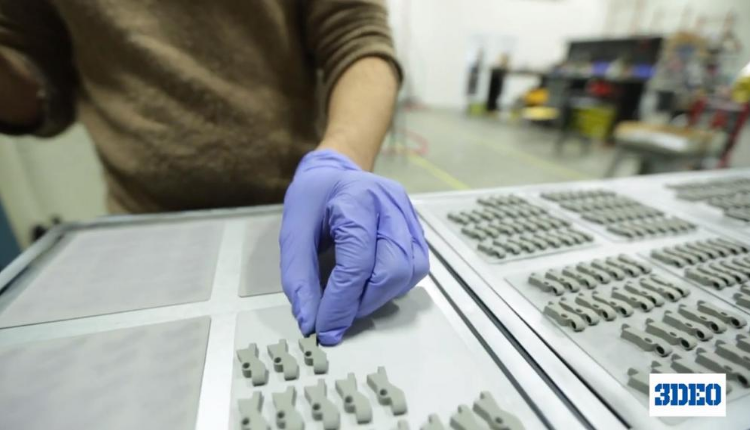 3DEO More Than Doubles Production Capacity in Q1 To Meet Demand A person wearing blue gloves inspects small metal parts arranged on a tray in a workshop.