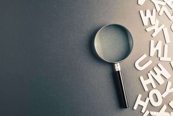 A magnifying glass lies on a dark surface next to scattered white alphabet letters, resembling a meticulous engineer's desk scattered with essential engineering terms.
