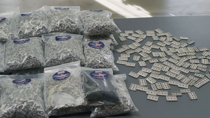 3DEO Ships 150,000 Production Parts, Breaking Ground in Metal Additive Manufacturing Several bags filled with small, white plastic pieces are laid on a gray table. Next to the bags, numerous individual plastic pieces are scattered.