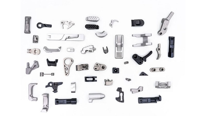 2021 Year in Review: 3DEO Sets Records in Metal 3D Printing for Mass Production A collection of various metallic and plastic mechanical parts laid out on a white background.