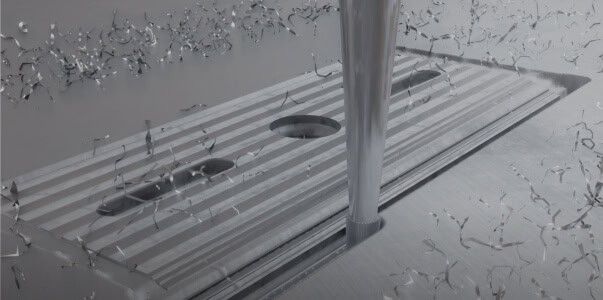 A close-up of a CNC machine drilling into a metal surface, creating spiral metal shavings. The metal workpiece, enhanced by metal 3D printing, has several holes and grooves already machined into it.