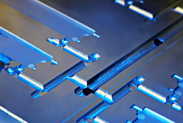 Close-up of a metallic, industrial component with complex geometric shapes and a blue tint, crafted using MIM technology.