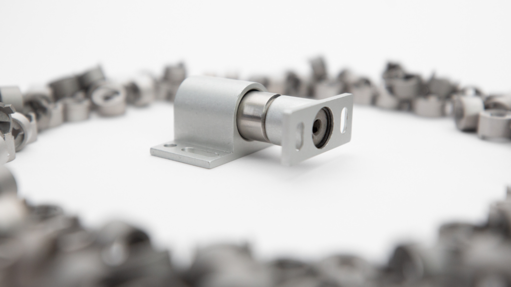 Metal sliding door roller hardware on a white surface, surrounded by blurred metal coils in the background, showcasing the ingenuity of US based manufacturing.