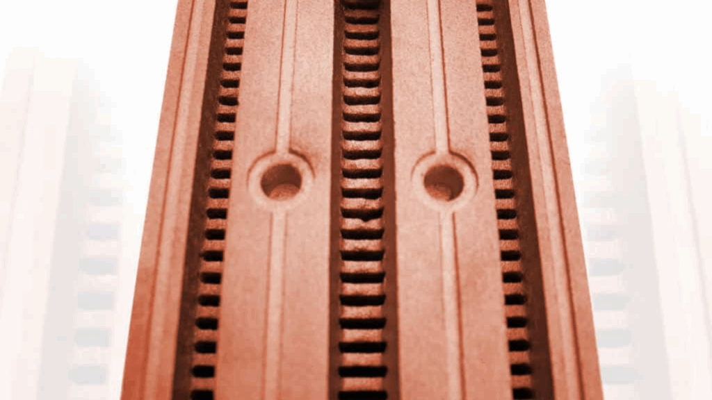 Close-up of a reddish-brown grooved and perforated pure copper surface with two round holes, likely part of an industrial or mechanical component.